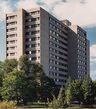Tall multi-story grey apartment building with green trees in the foreground.