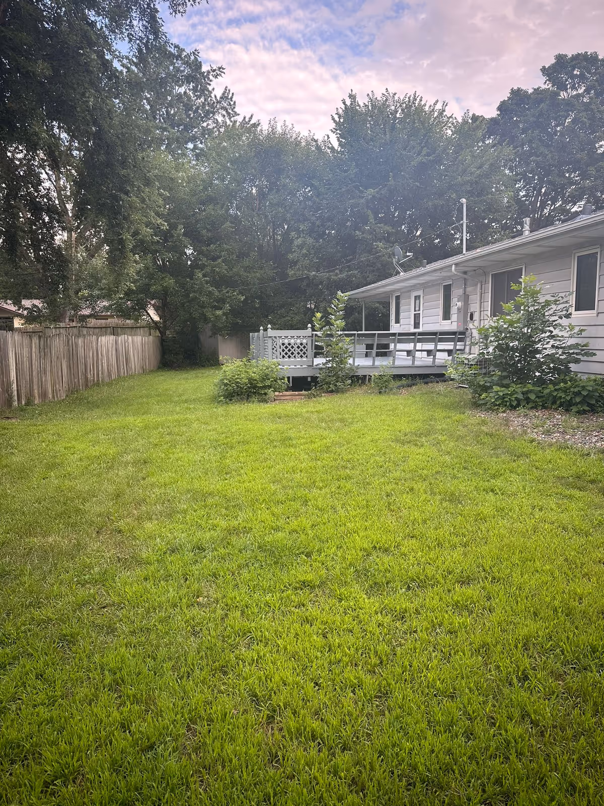 Lush backyard lawn beside a single-story building with a wooden deck.