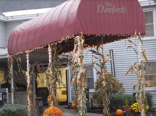 Entrance to Danforth Adult Care Center with maroon canopy, string lights, and fall decor.