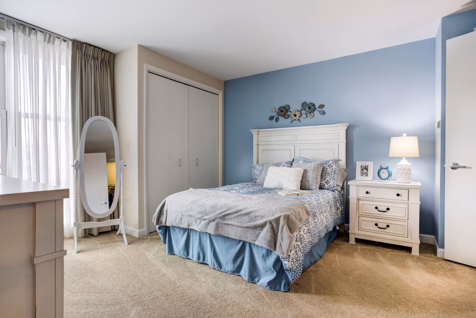 A cozy bedroom in a senior living facility featuring a white bed and blue accent wall.