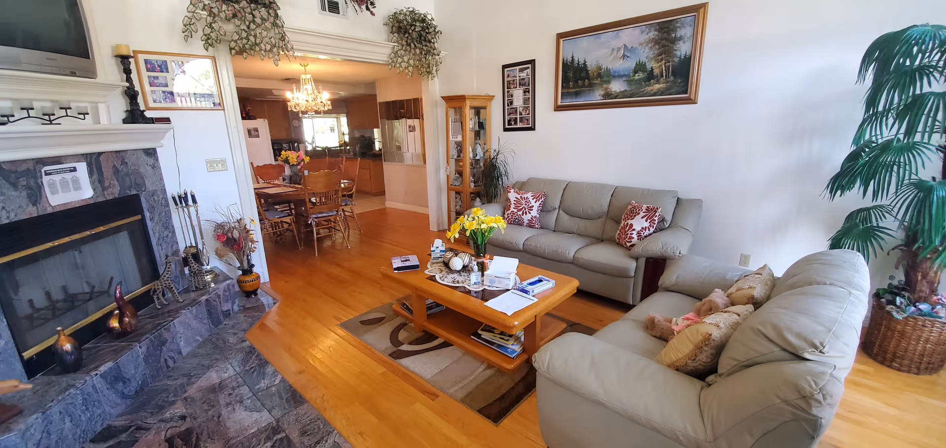 Cozy living room in a senior facility with beige sofas, fireplace, and wooden floors.