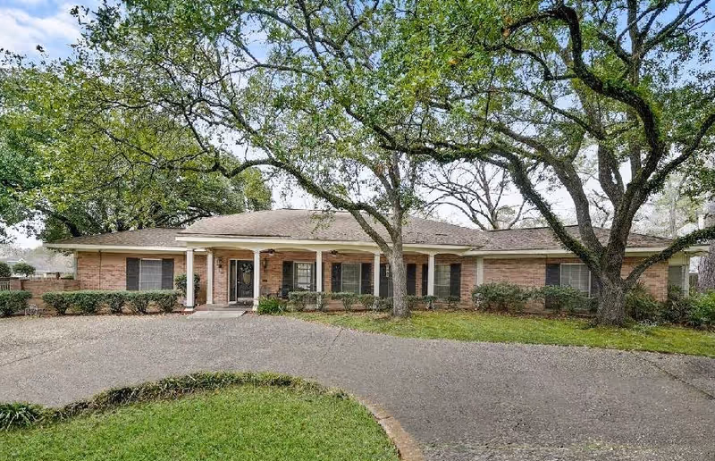 Single-story brick facility with a shaded entrance, mature trees, and a curved gravel driveway.