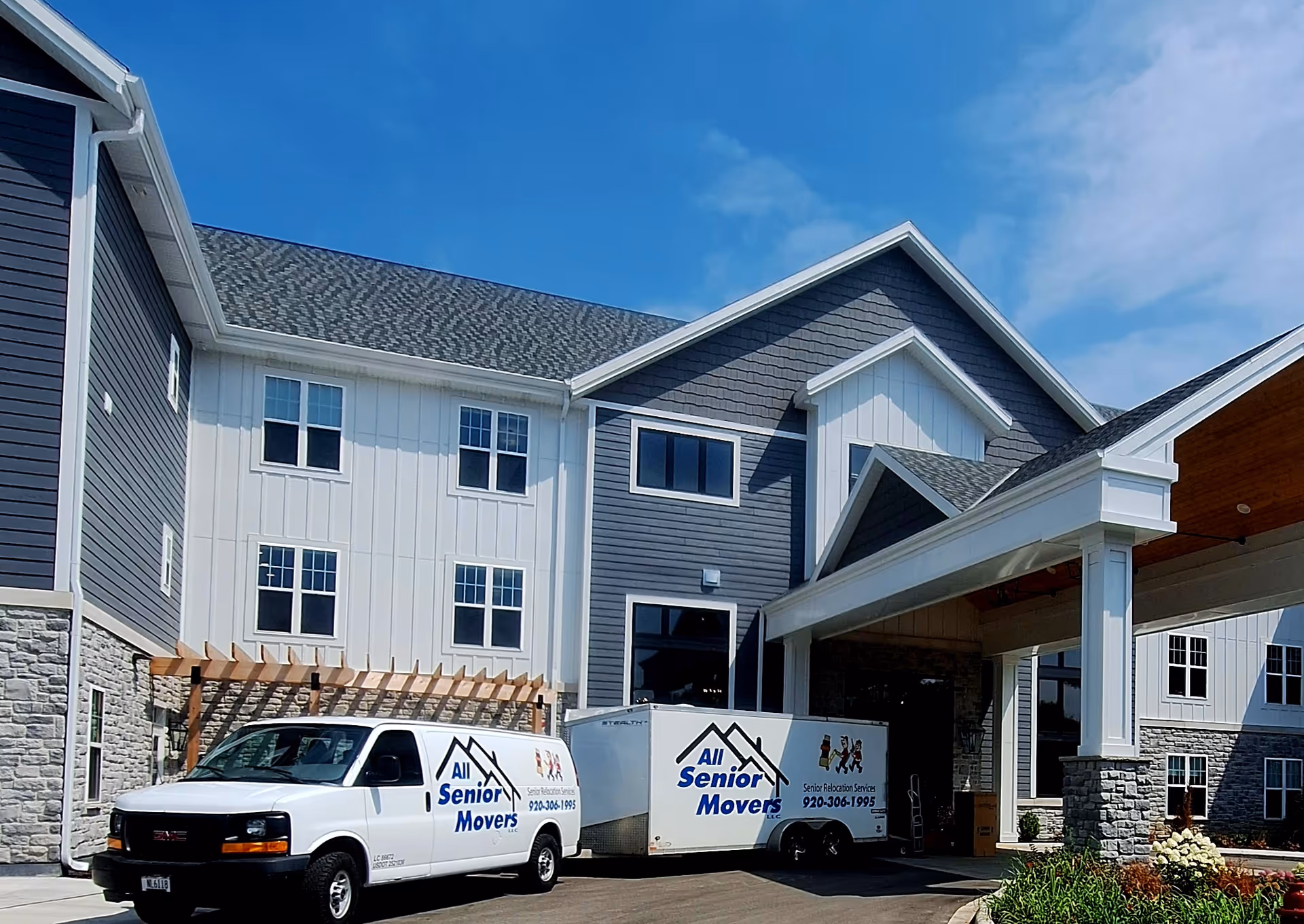 Exterior view of a senior living facility with a covered entrance and two white moving vans.