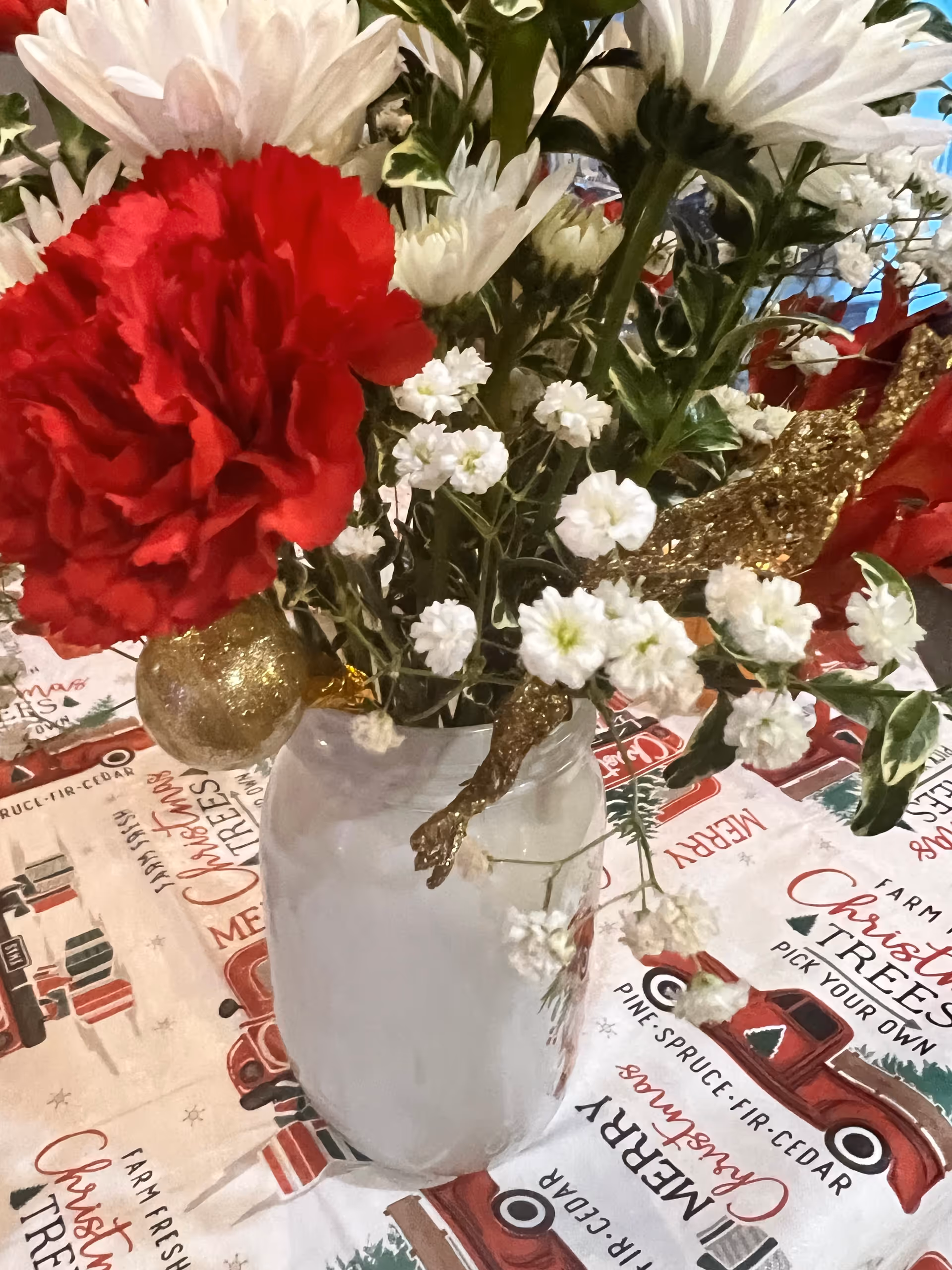 A white vase filled with red and white flowers as a holiday centerpiece on a festive tablecloth.
