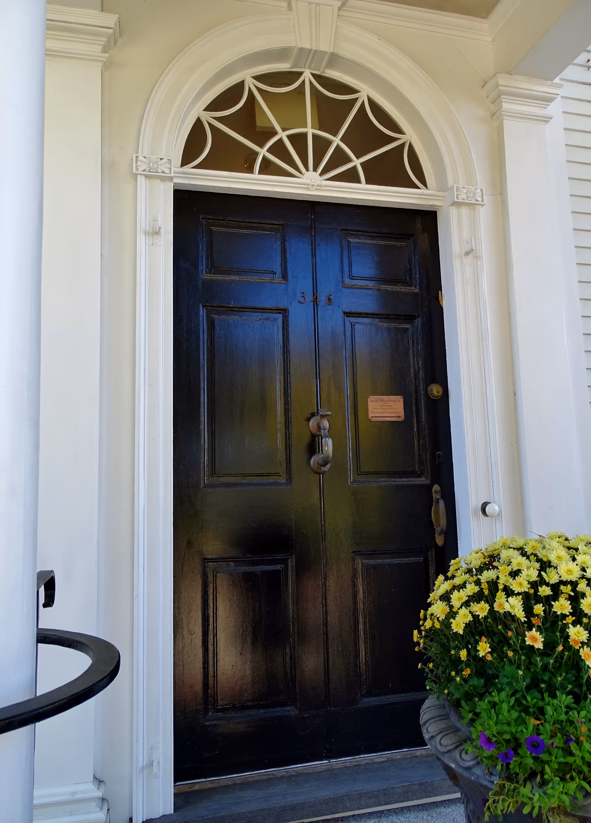 Black front door with arched window, white trim, and potted yellow flowers at entrance.