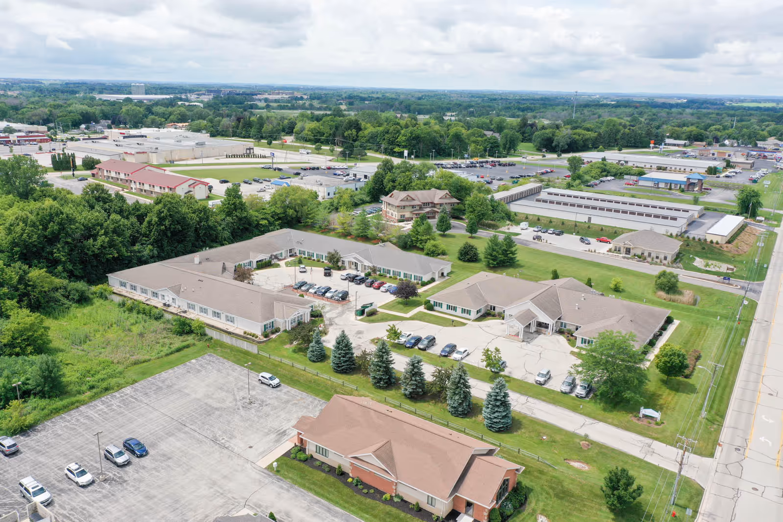 Aerial view of a senior living campus with beige buildings, green lawns, and parking lots.