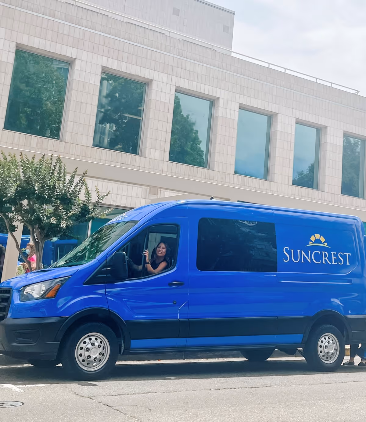 Blue Suncrest van parked in front of a modern building.