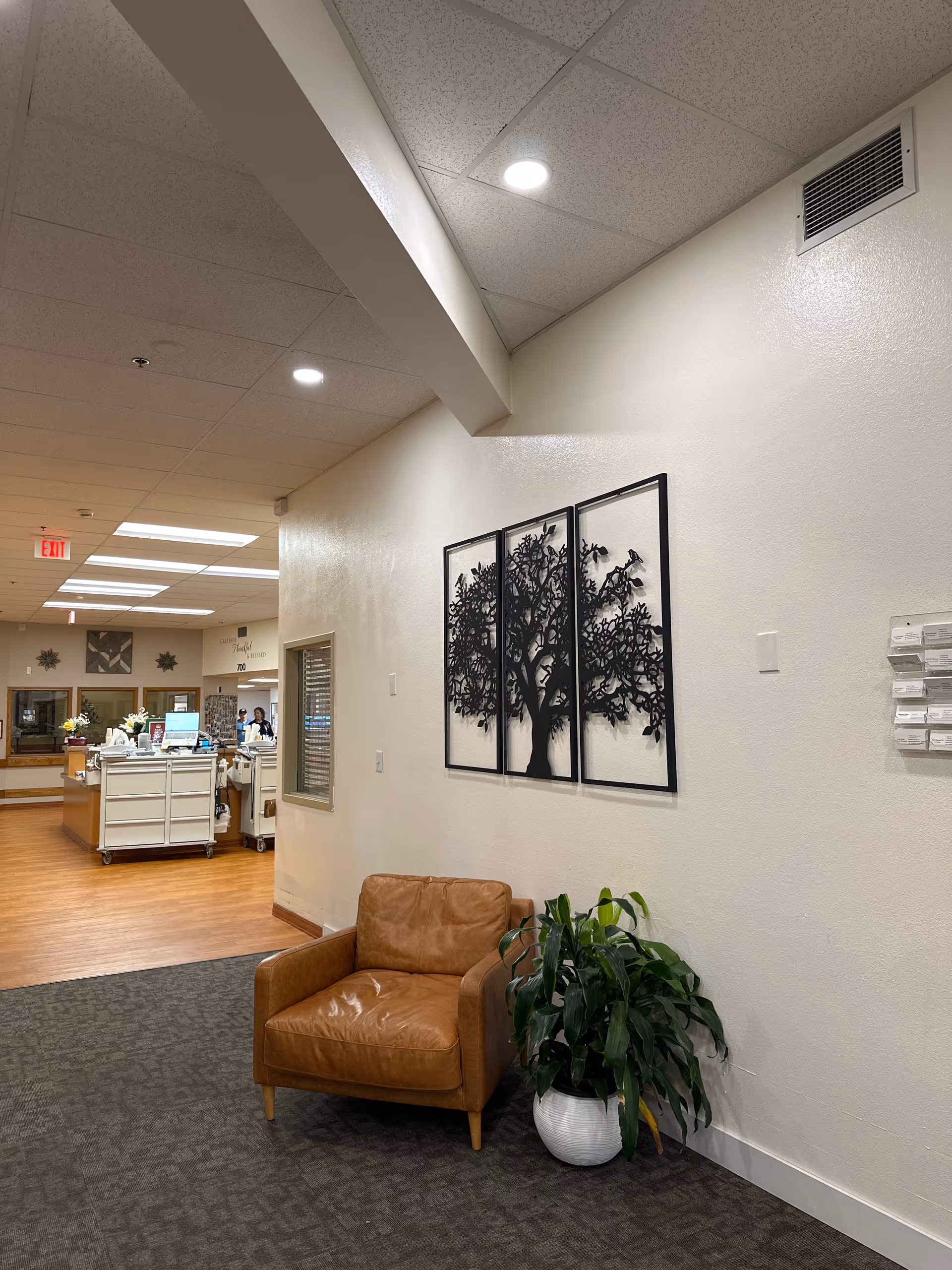 Lounge area in a hallway with a brown leather chair, plant, and wall art.