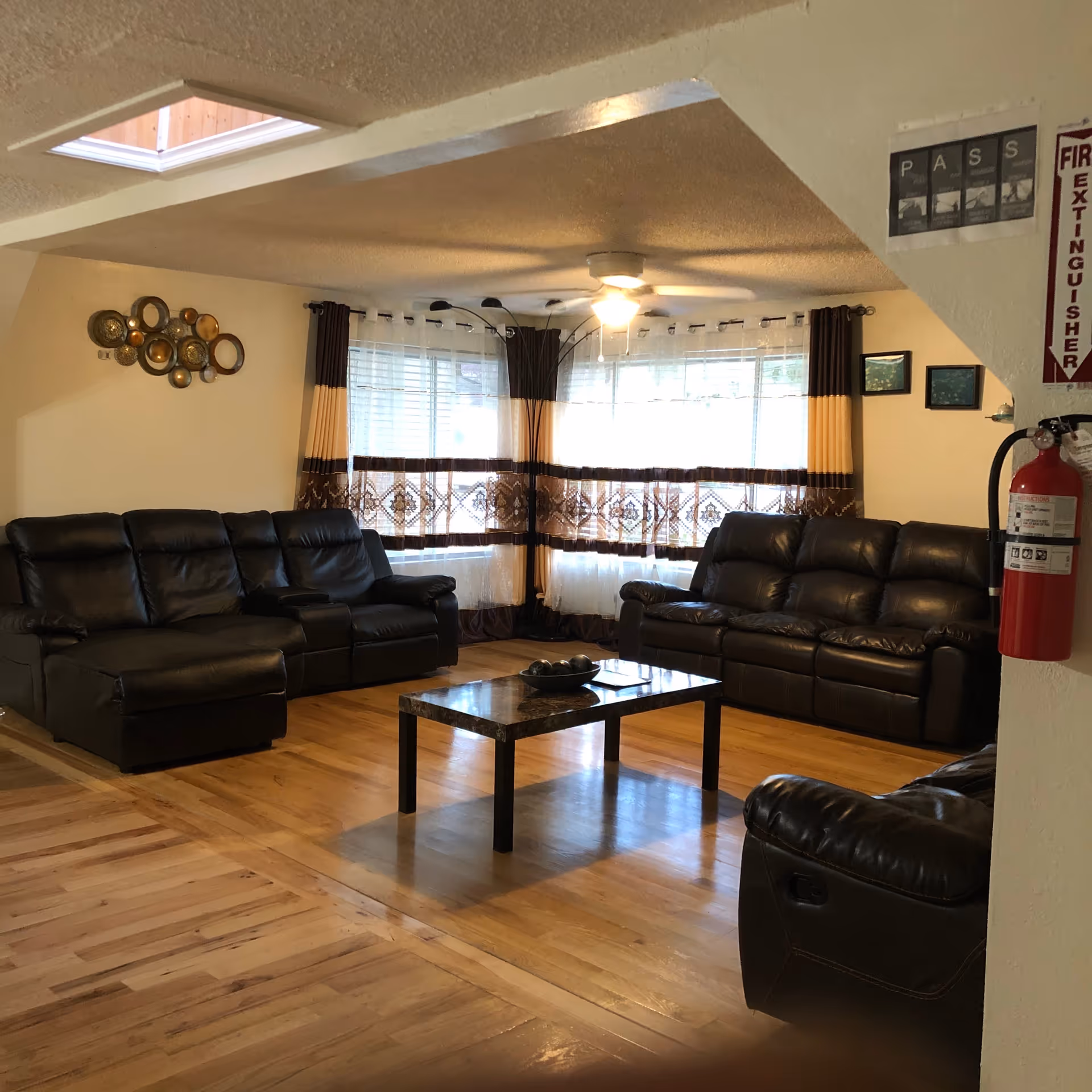 Senior living facility living room with black leather sofas, wood floor, and large windows.