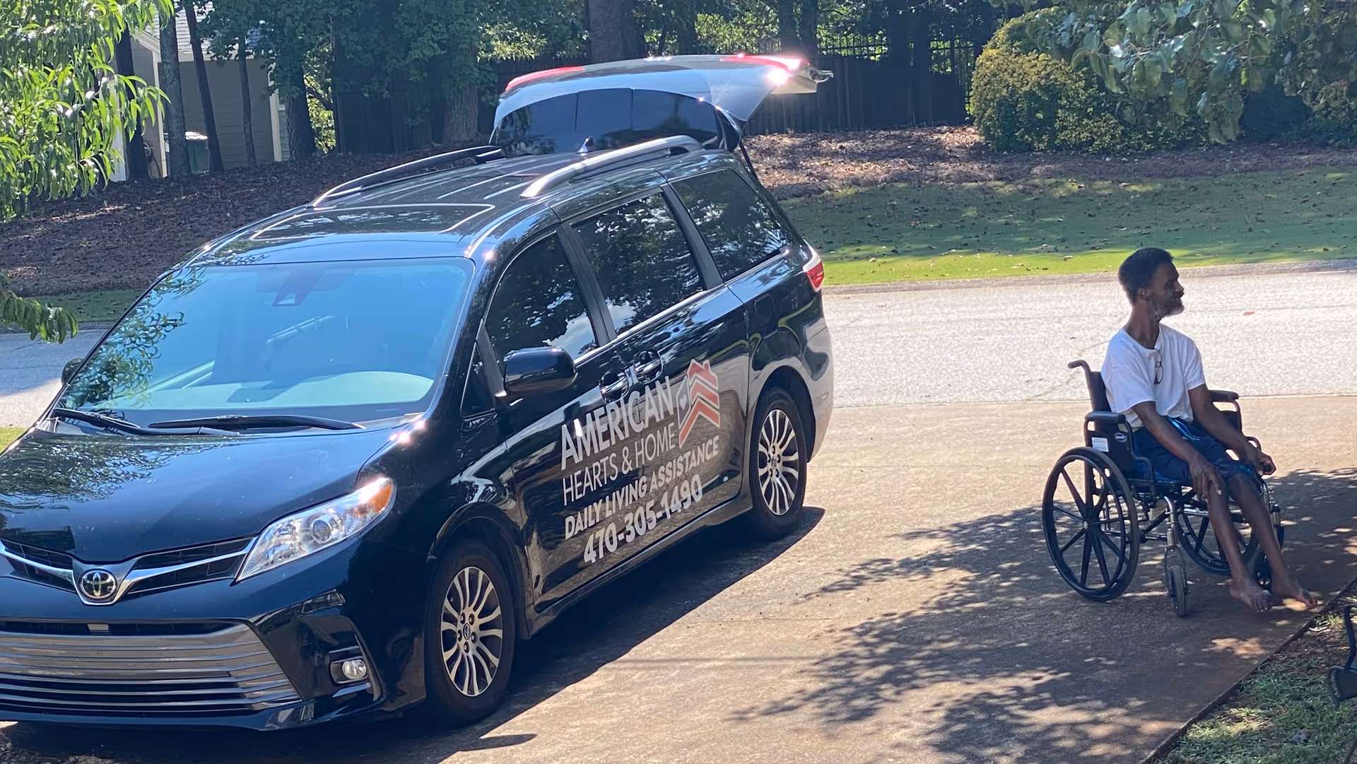 A black van labeled American Hearts and Home sits near a man in a wheelchair.