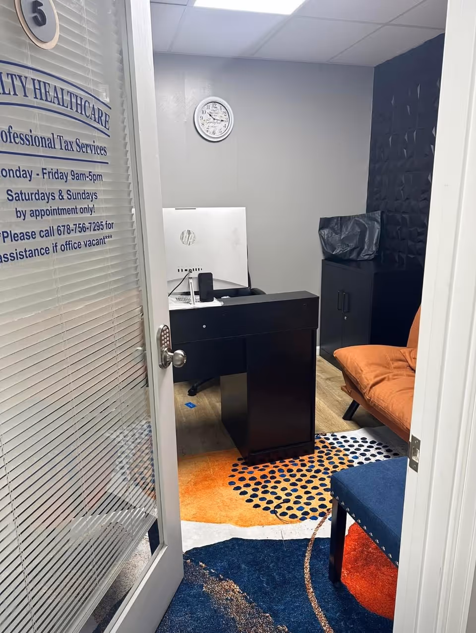 Interior office/reception area with desk, computer, clock, and colorful carpet.
