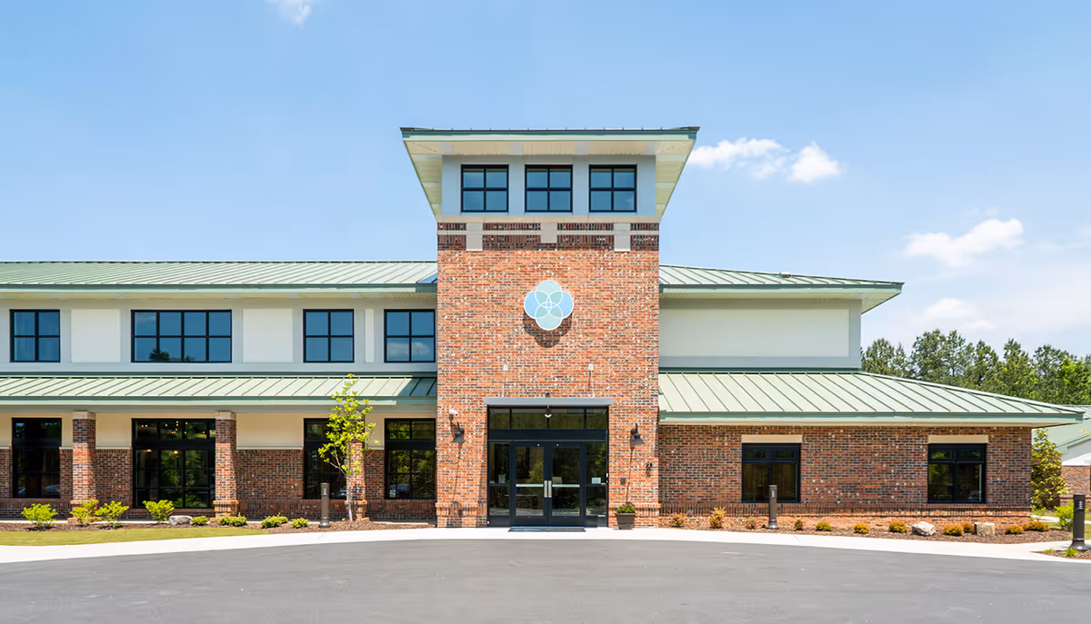Front exterior view of The Memory Center building with a brick facade, large windows, a green metal roof, and a clear blue sky above.