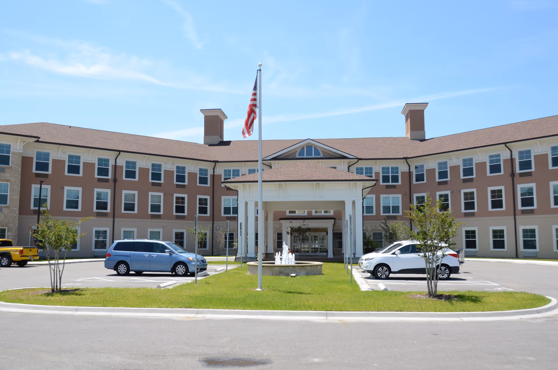 A senior living facility with a U-shaped brick exterior, flagpole, fountain, and circular driveway.