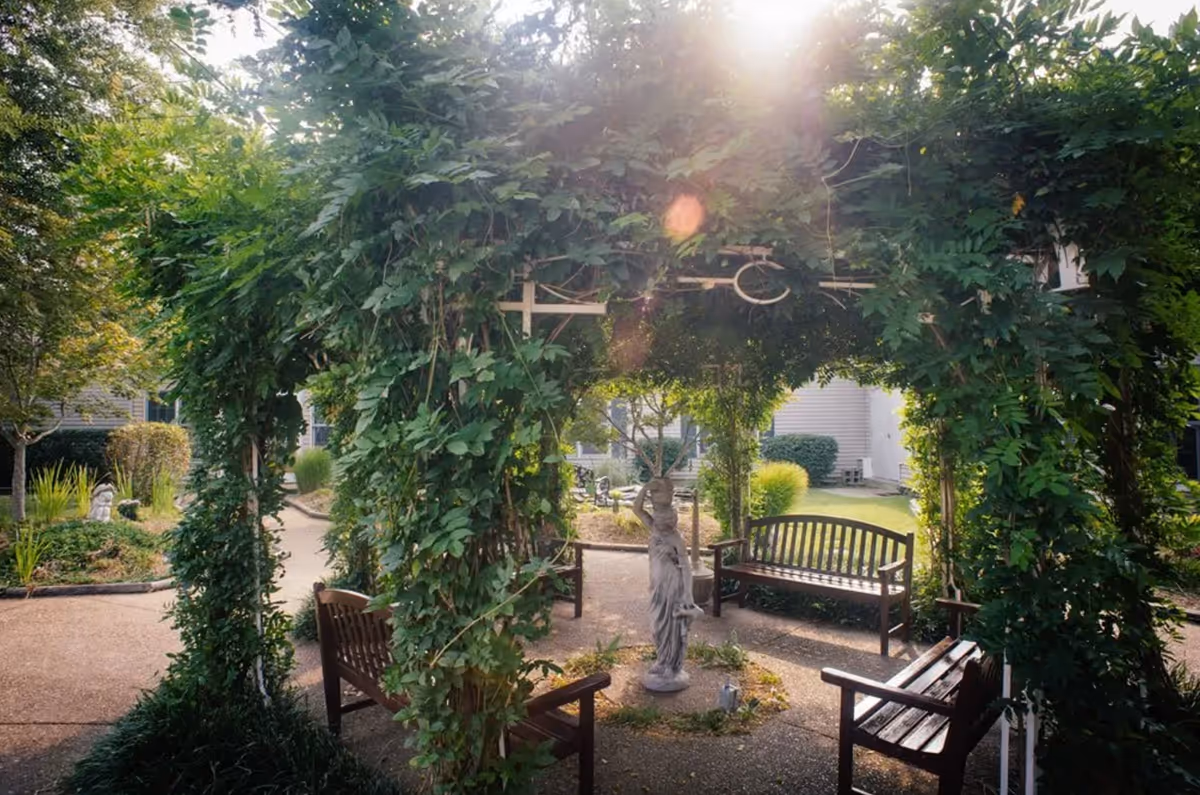 Outdoor courtyard at Gaither Suites with a vine-covered arch, benches, and a statue.