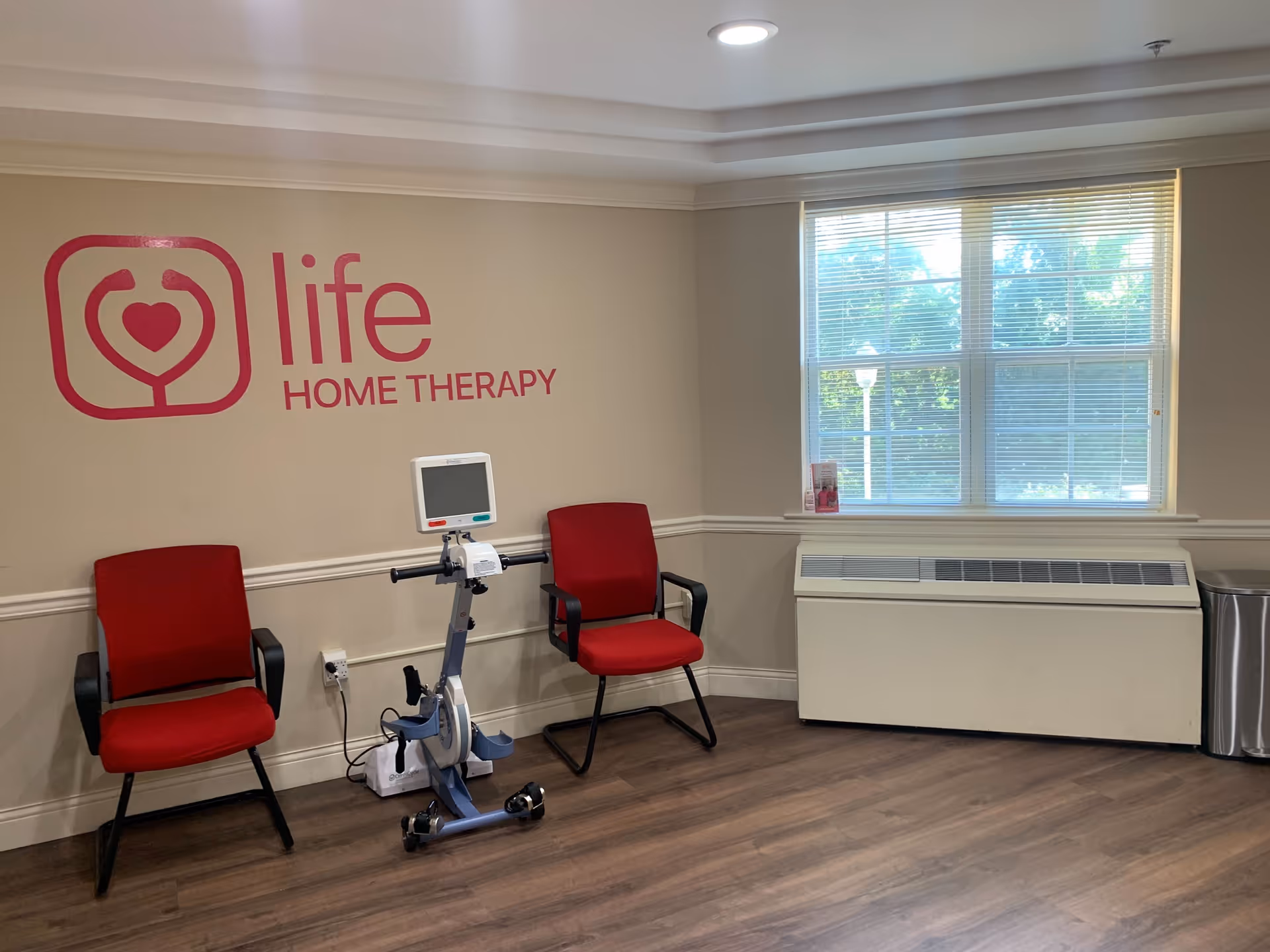 Therapy room with two red chairs, exercise bike, and Life Home Therapy logo on wall