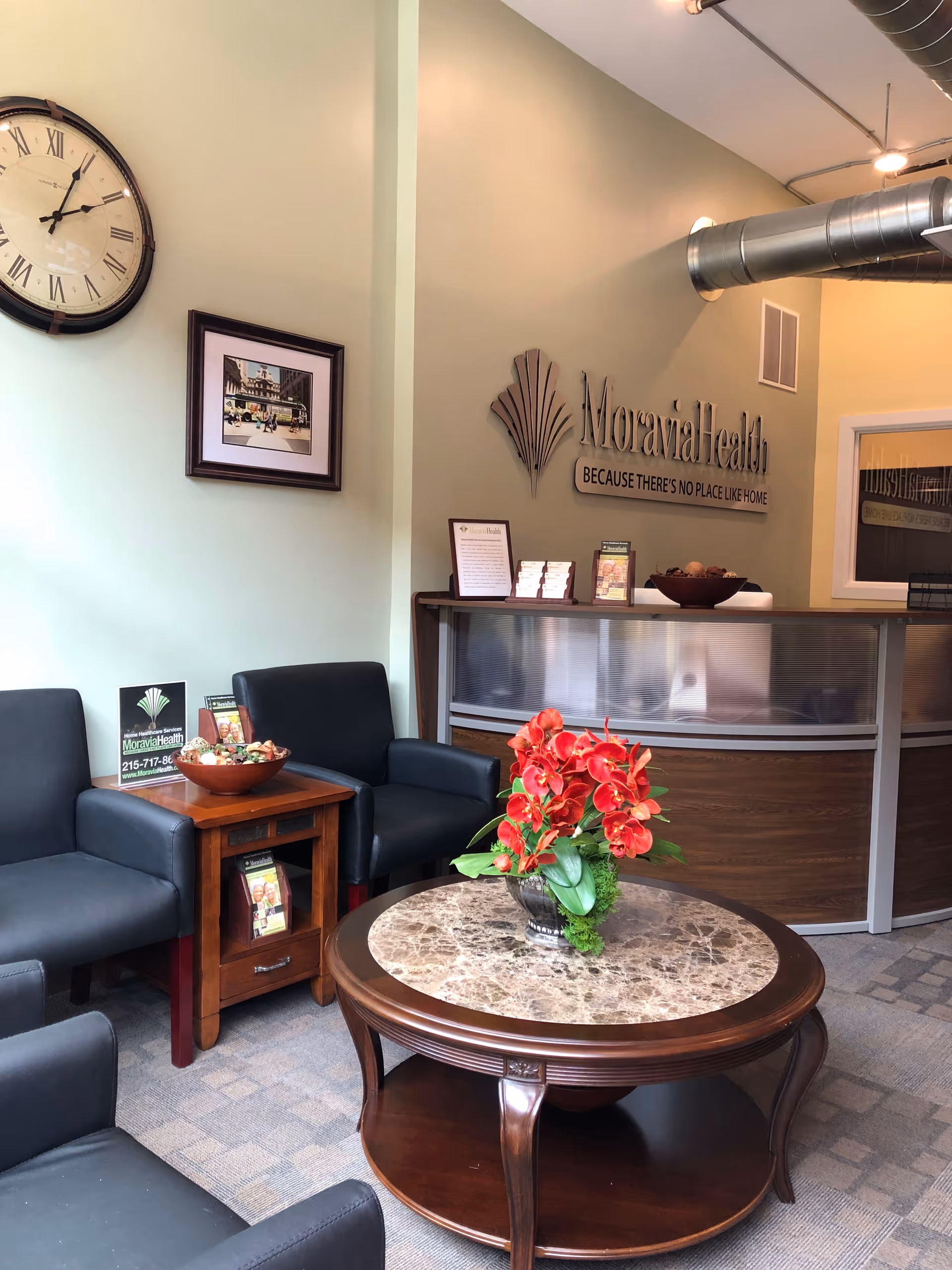 Lobby seating area with a reception desk, clock, and red flower arrangement.