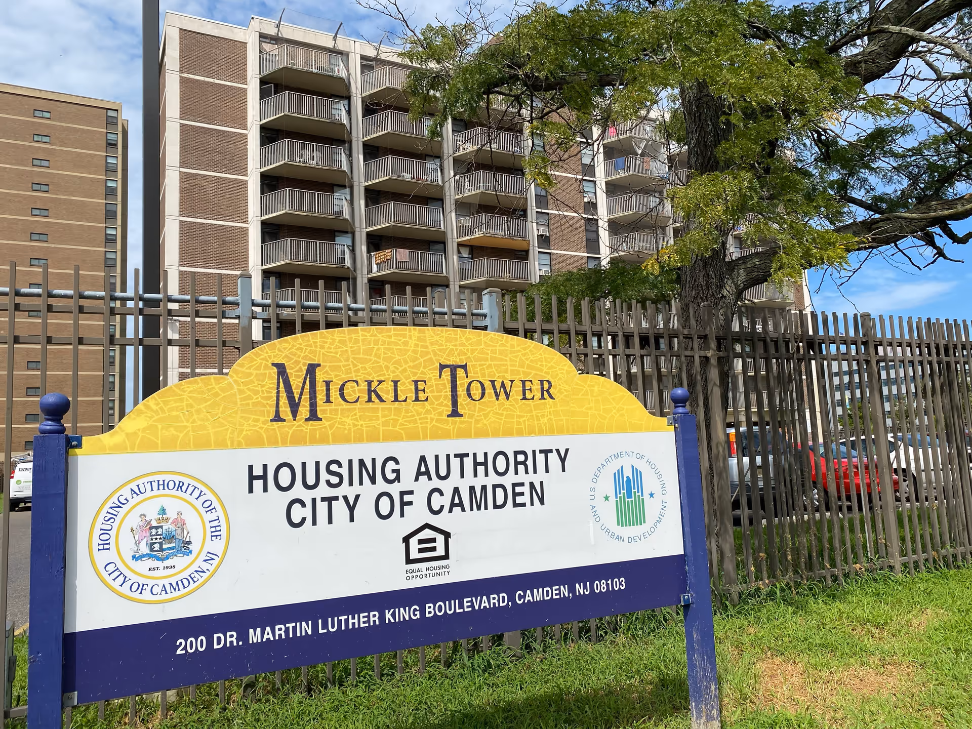 Front view of Mickle Tower sign with a high-rise building behind a metal fence.