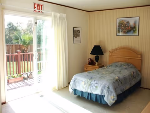 A bedroom in a care home with a single bed and door to an outdoor deck.