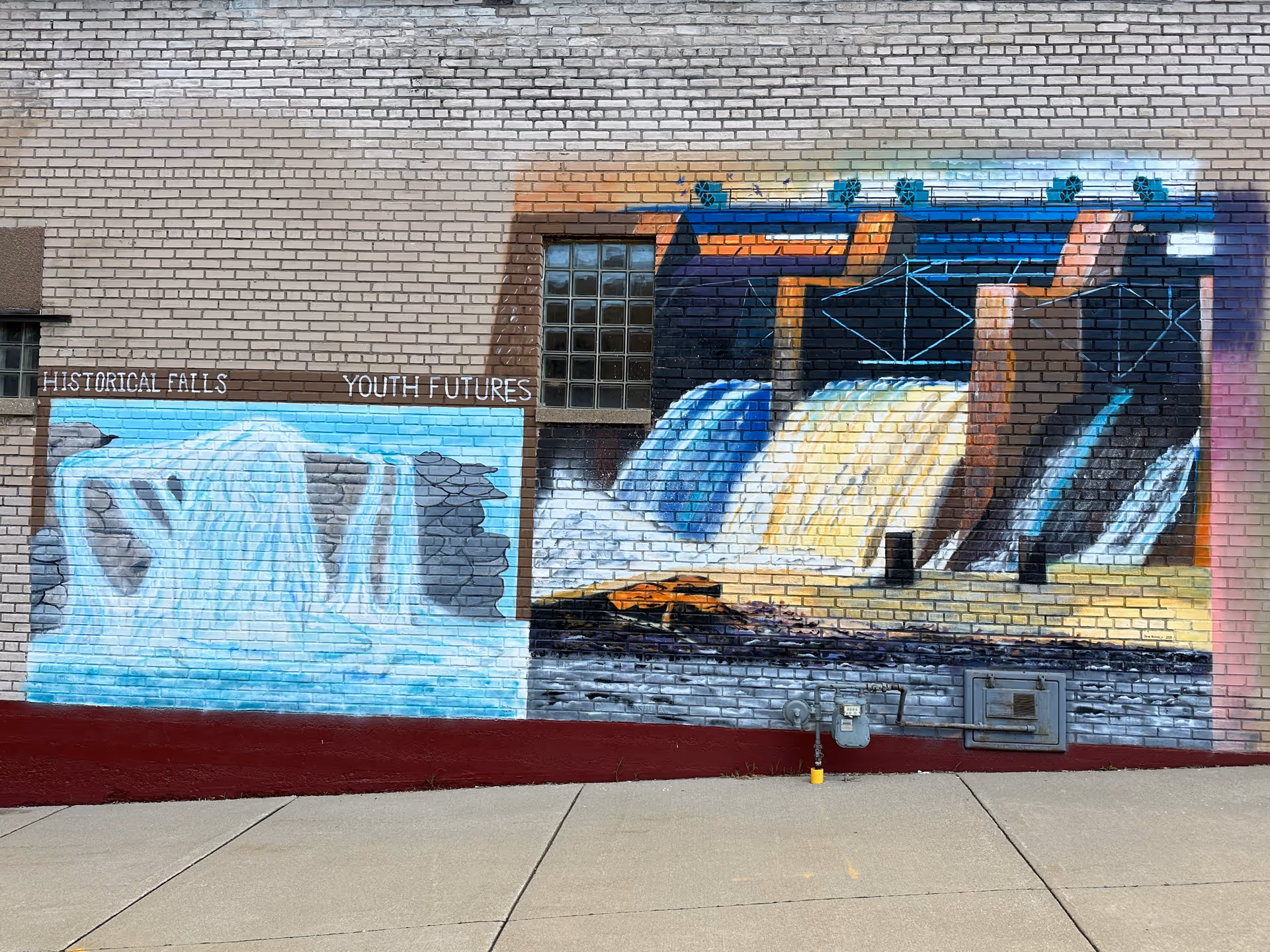 Brick exterior wall with large colorful waterfall mural and graffiti, no people.