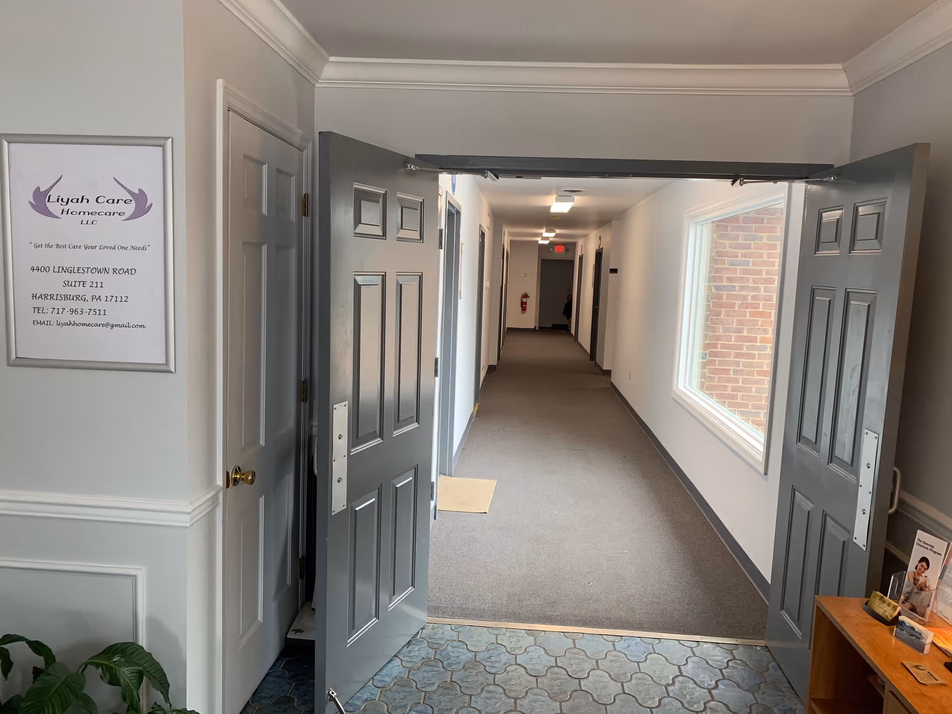 Open double doors reveal a long, well-lit corridor with a window and sign.