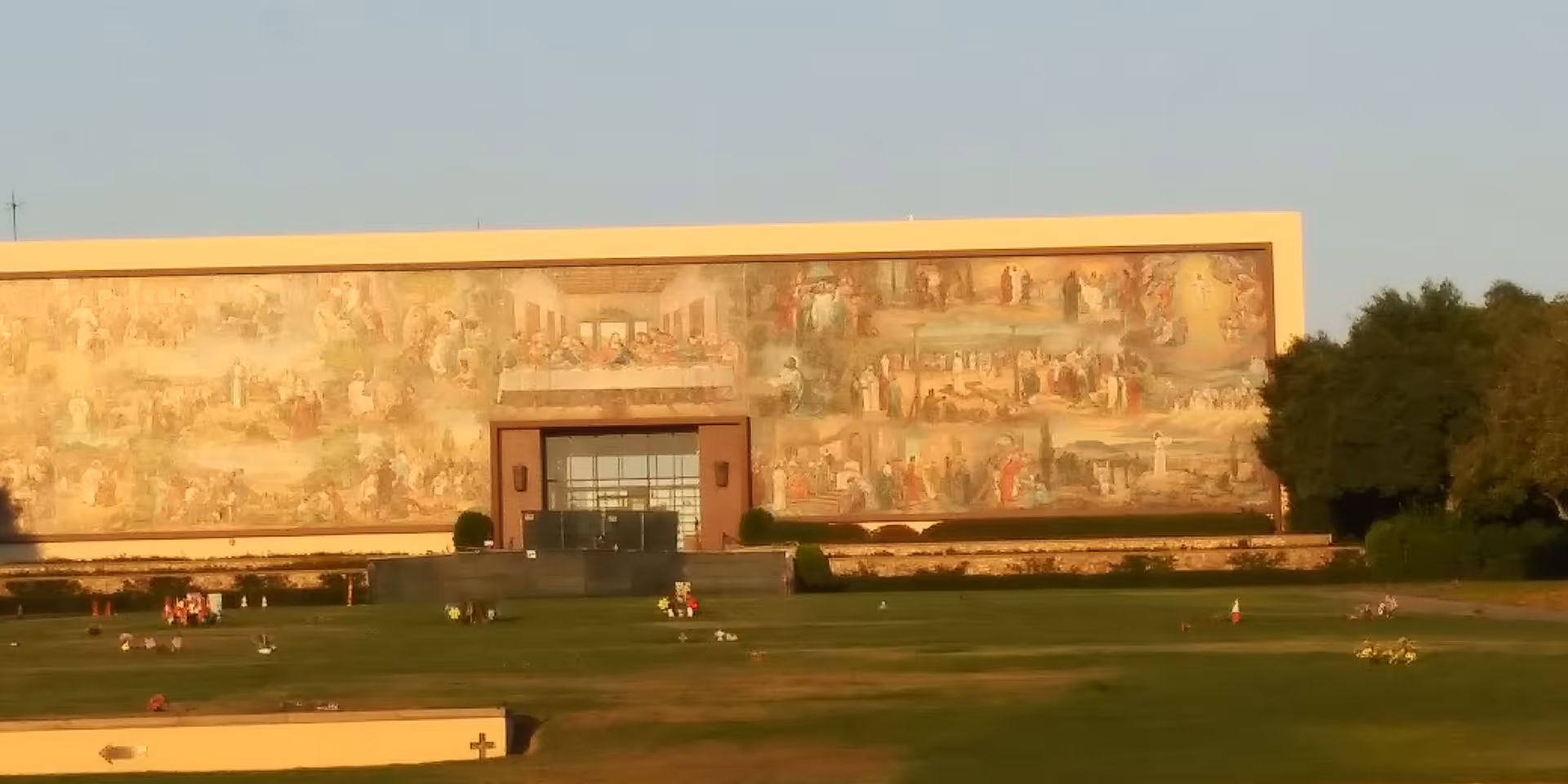A large building exterior with a mural, entrance doors, and a manicured lawn in front.