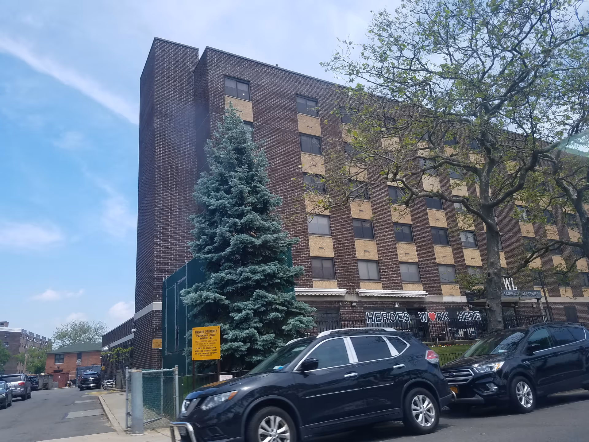 Brick, multi-story senior care building facing the street with cars parked.