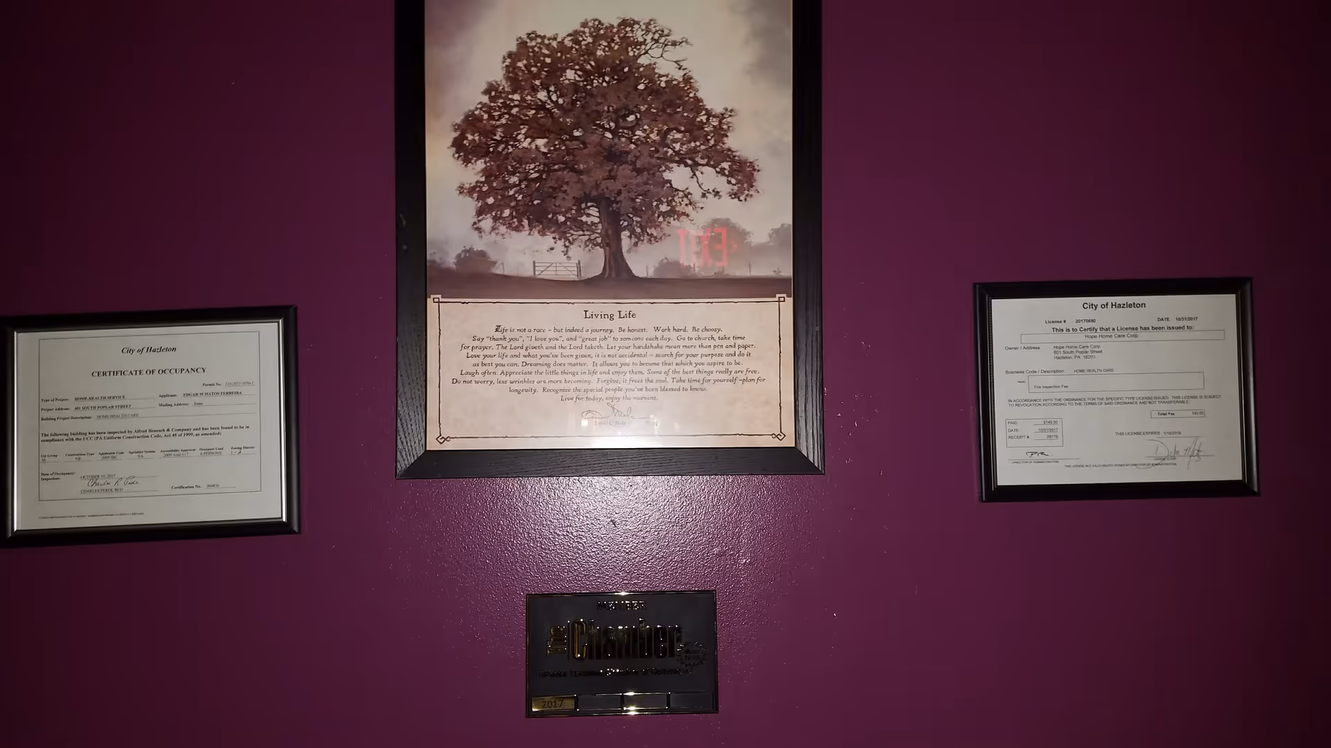 Purple wall featuring a tree art piece flanked by framed certificates.