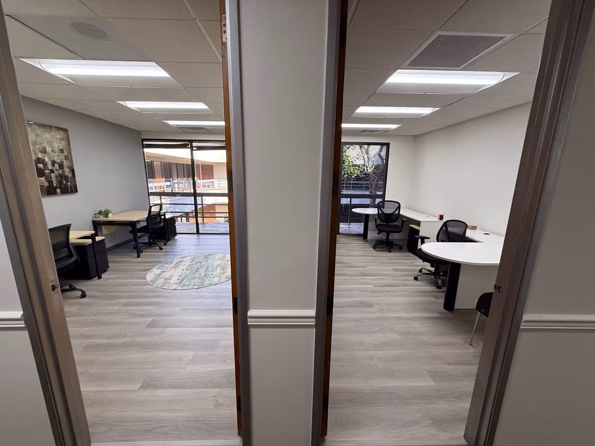 Interior view of two office spaces with desks, chairs, and large windows.