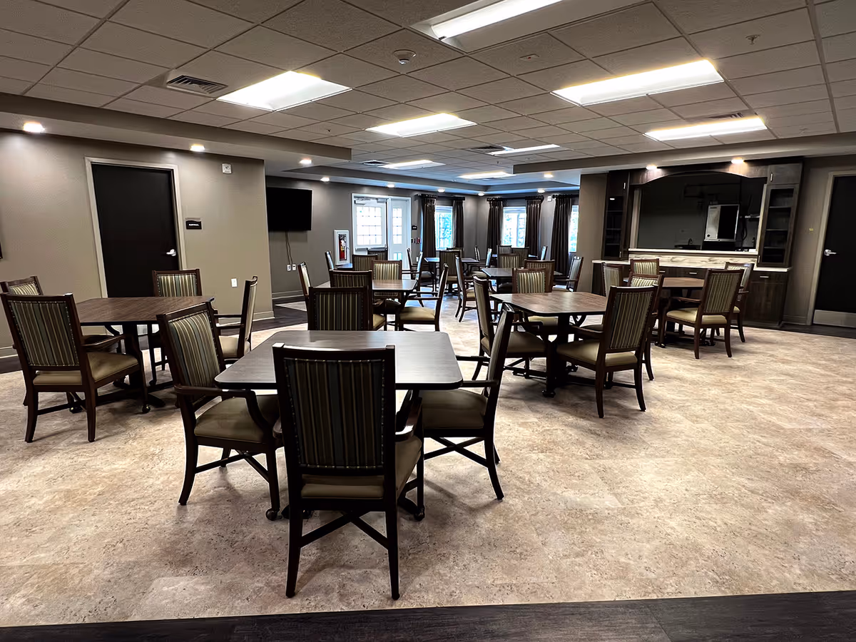 Spacious indoor dining hall with multiple tables, chairs, and a kitchen/bar area in the background.