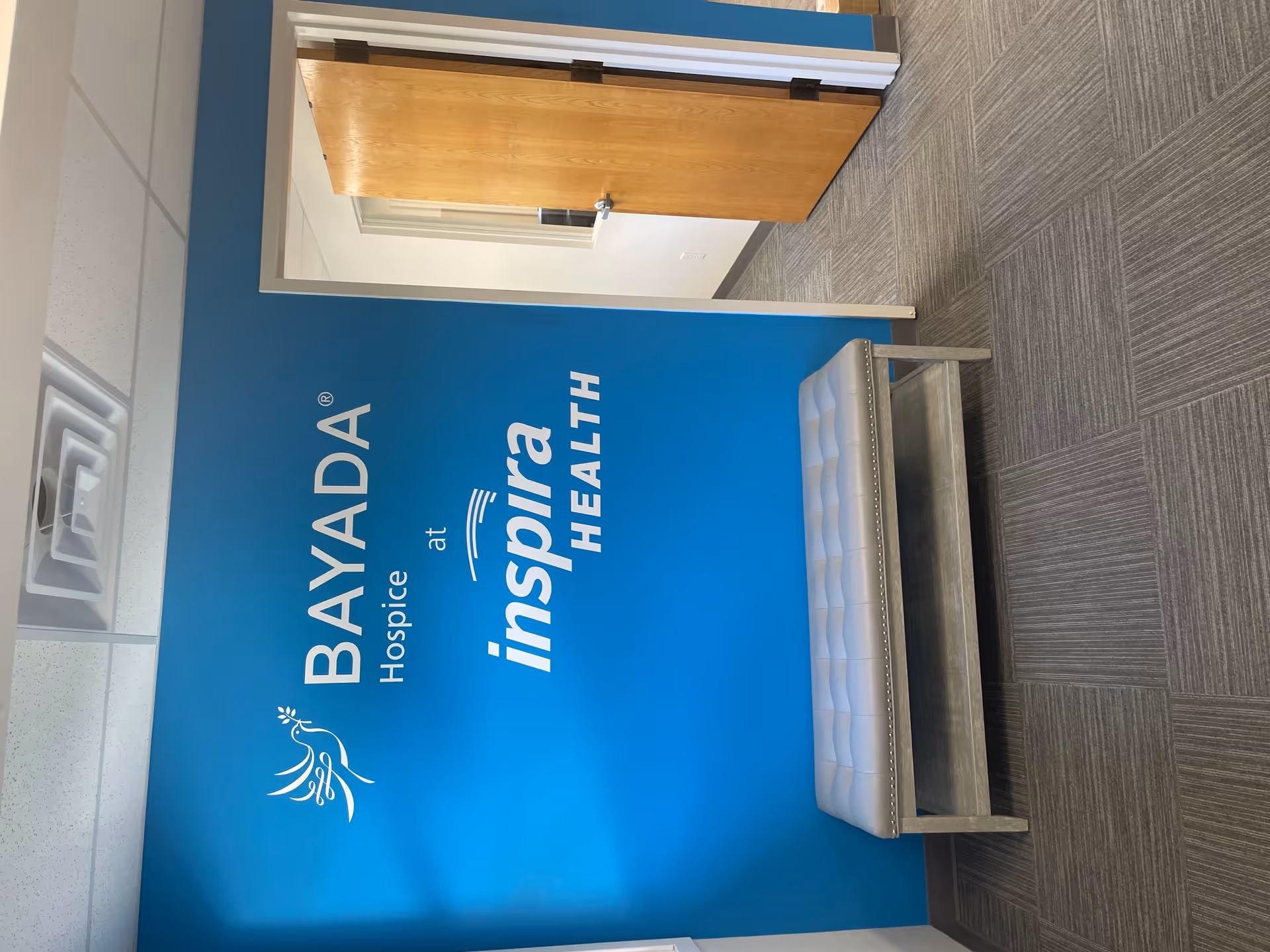 Blue wall with BAYADA Hospice and Inspira Health branding beside a small gray bench.