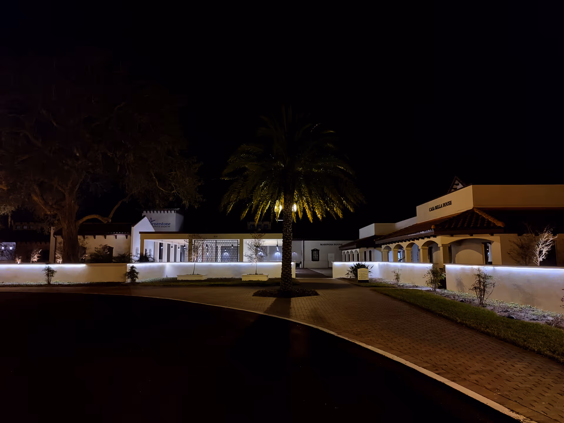 Night view of Cornerstone Hospice & Palliative Care exterior with palm trees and walkway lighting.