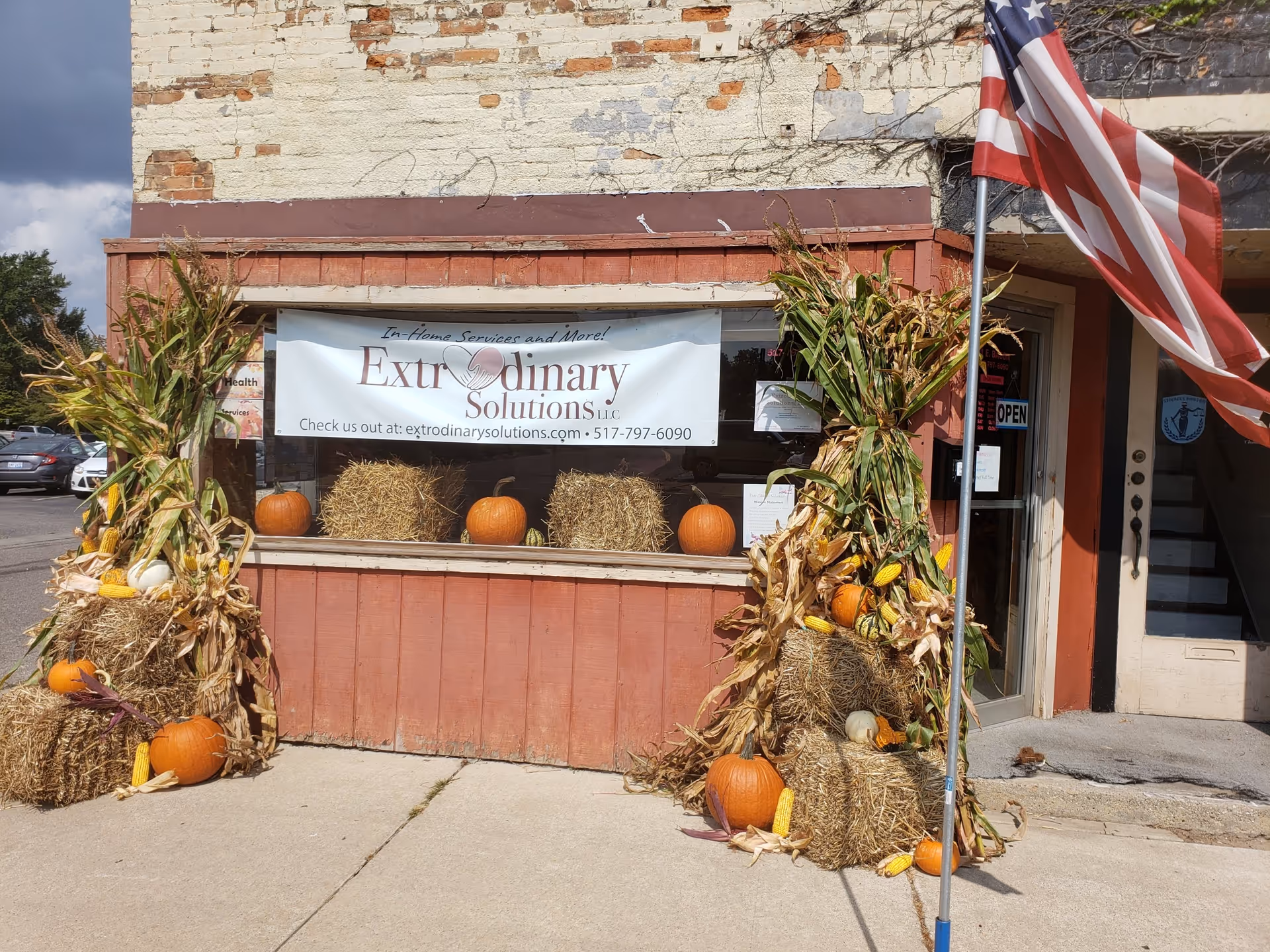 Storefront display with pumpkins and hay bales, banner for ExtrOrdinary Solutions LLC, American flag.