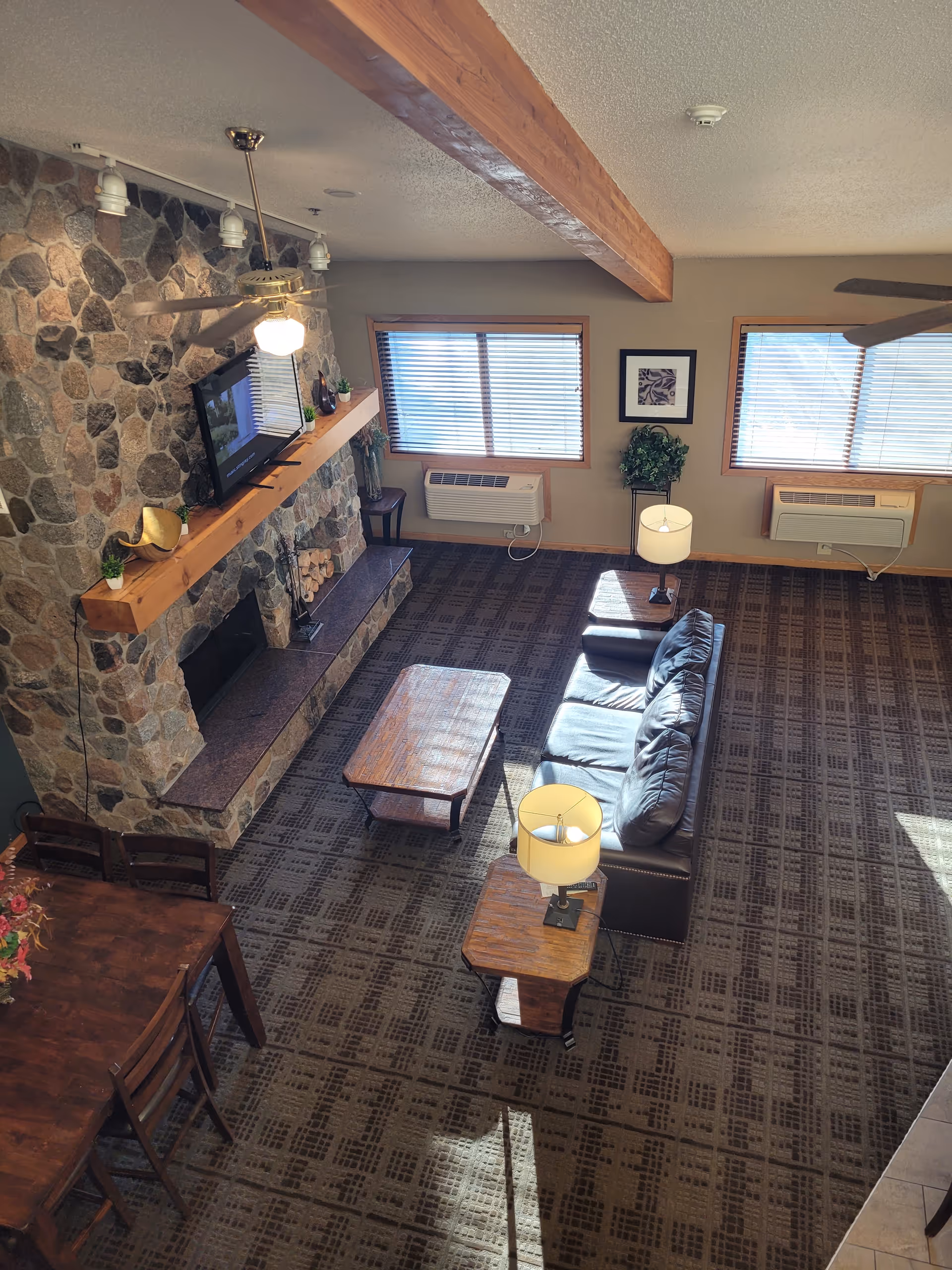 Cozy senior living lounge with stone fireplace, couch, tables, and windows.