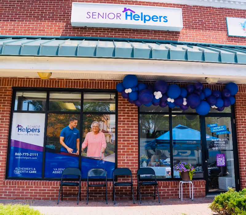 Brick storefront with Senior Helpers Central West Hartford sign, balloons, and outdoor seating.
