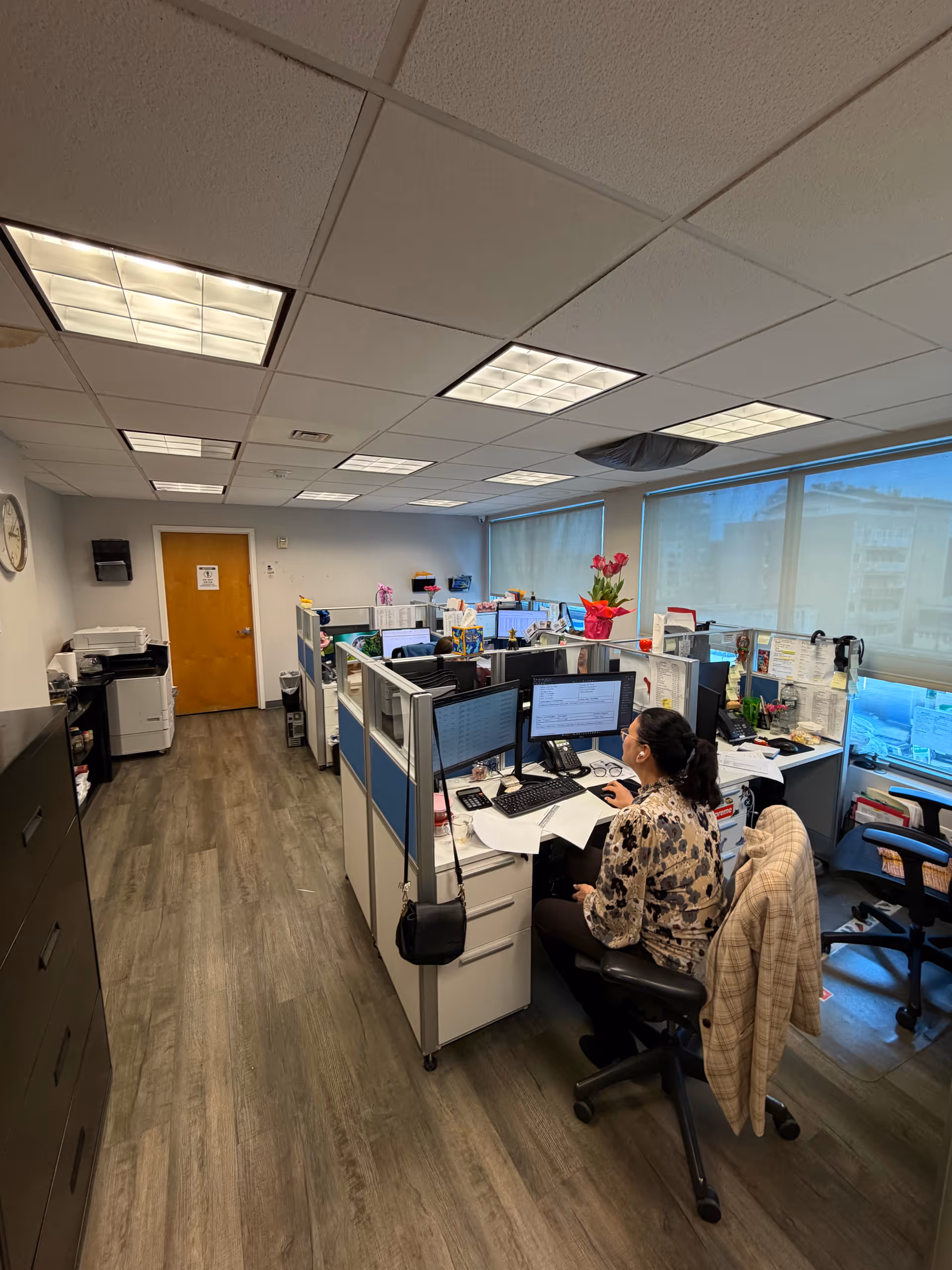 Office cubicles and a staff member working at a desk in a well-lit facility office.
