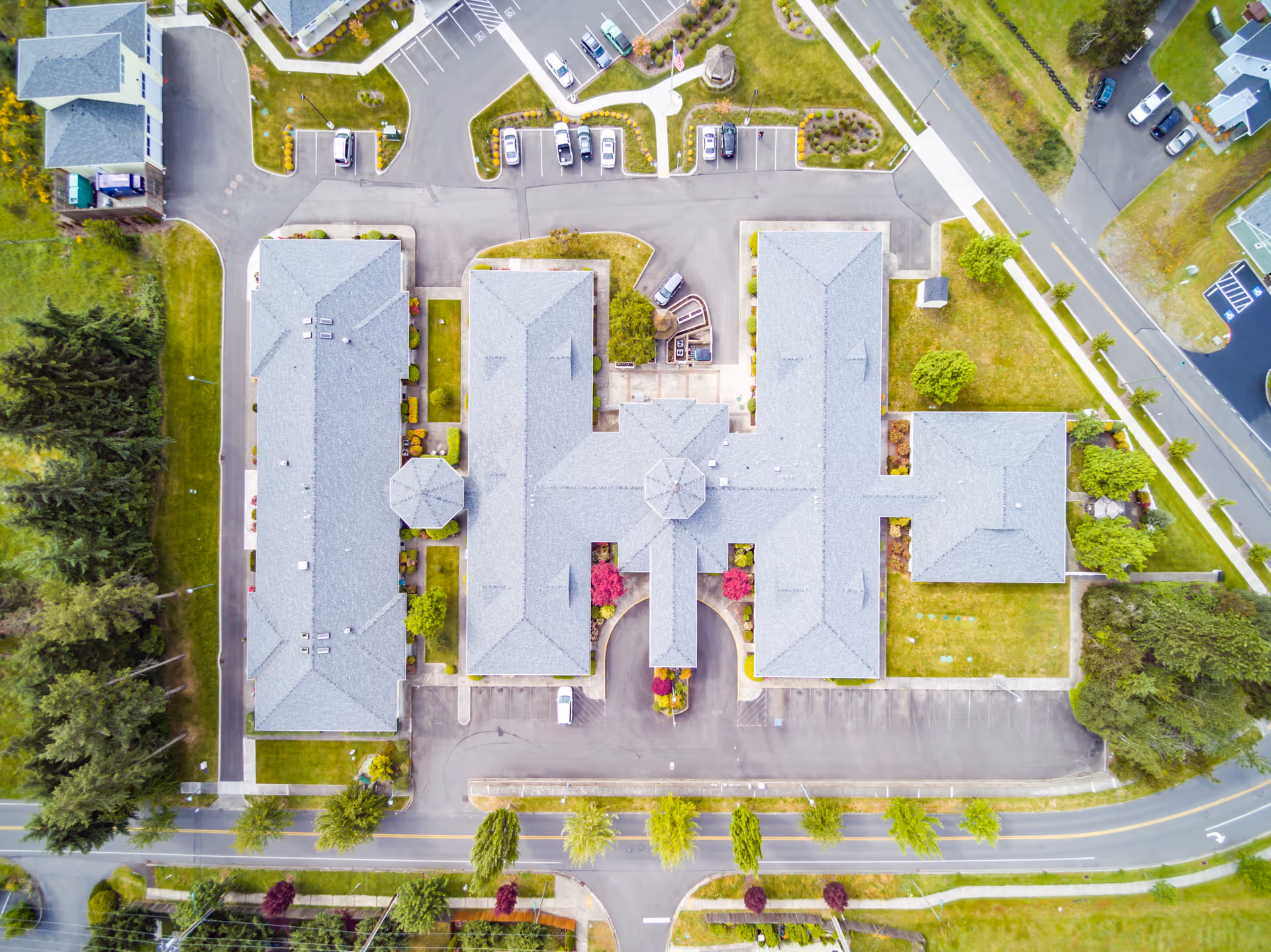 Aerial view of Easthaven Villa Assisted Living & Memory Care showing multiple connected buildings with gray roofs, surrounding parking lots, landscaped greenery, trees, and roads.