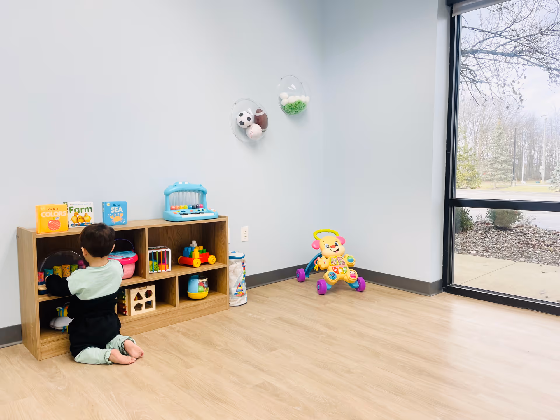 A child sits on the floor playing with toys in a bright playroom.