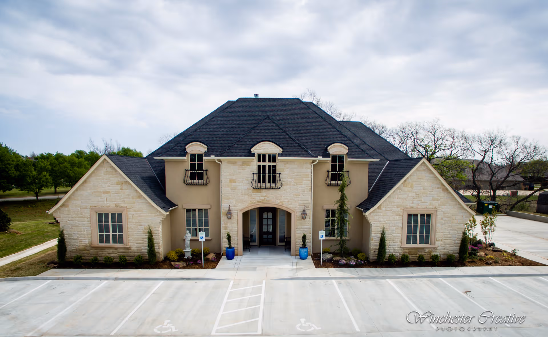 Exterior view of a beige stone senior living facility with a dark roof and front entrance.