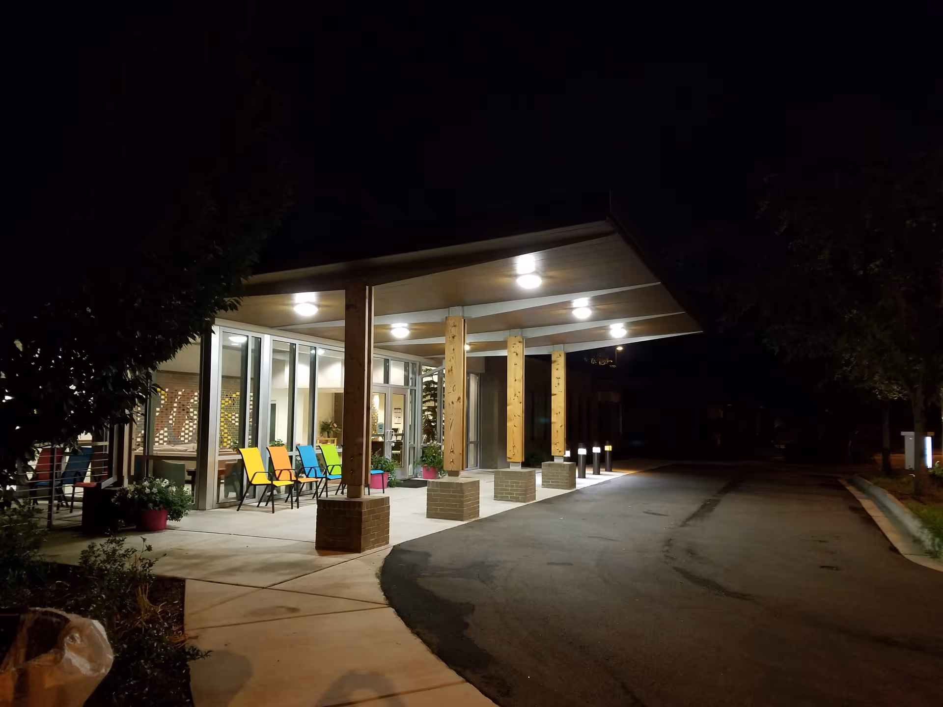 Night exterior of a senior living facility with colorful chairs outside a covered entrance