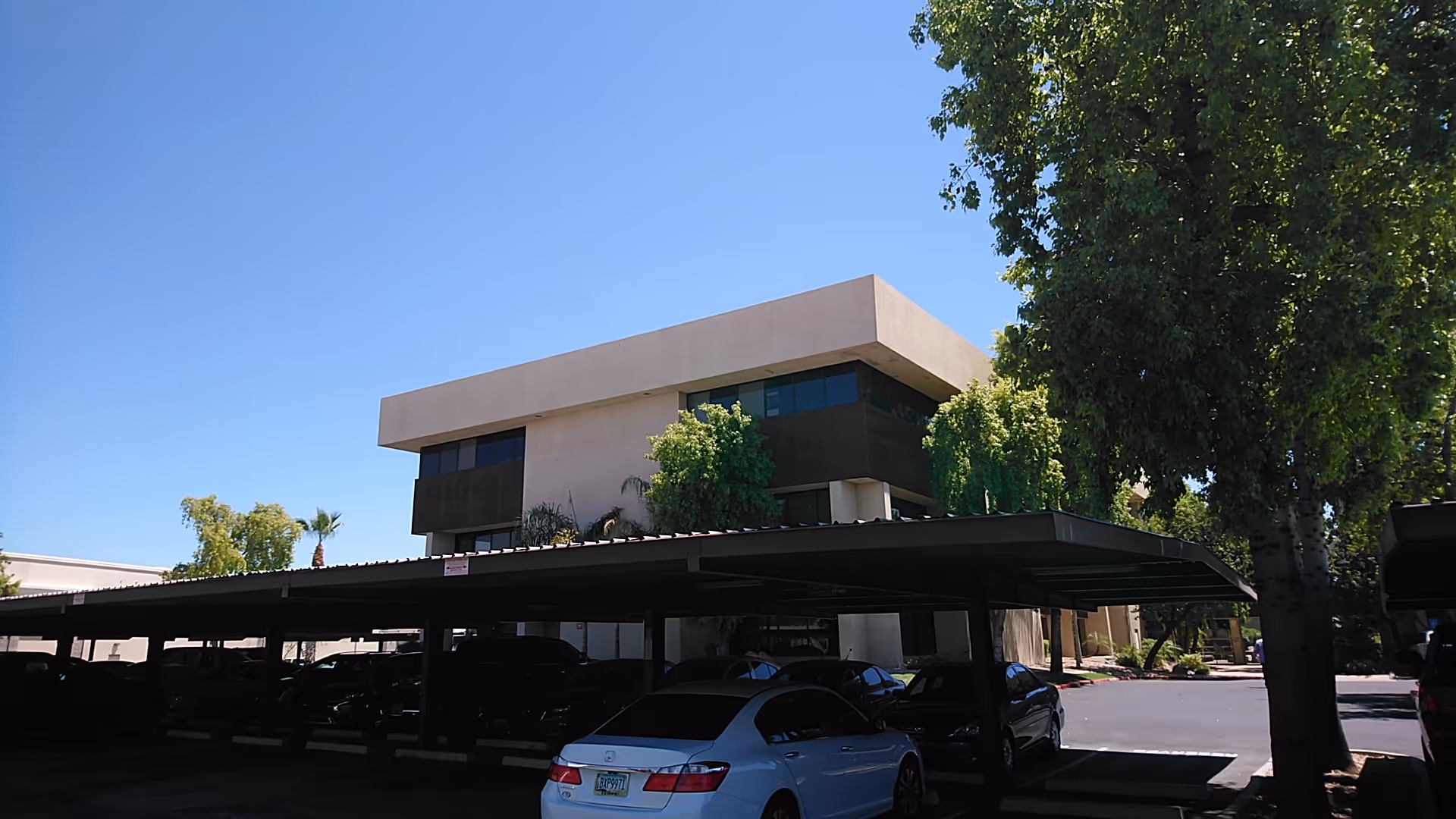 Senior living facility exterior with a long shaded parking area and trees.