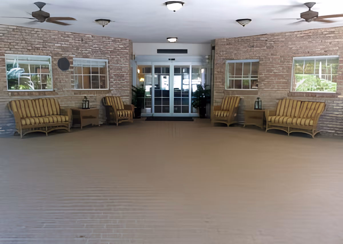Covered entrance area with wicker benches and chairs flanking glass double doors beneath ceiling fans.