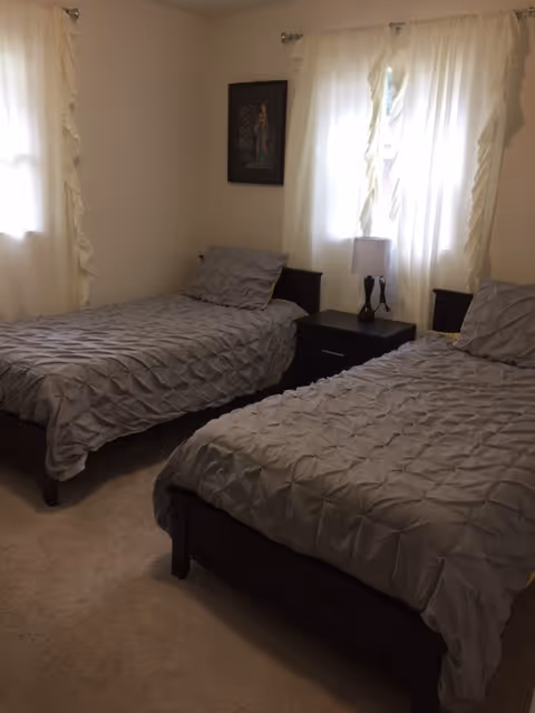 Shared bedroom with two twin beds, gray quilts, and a nightstand between them.