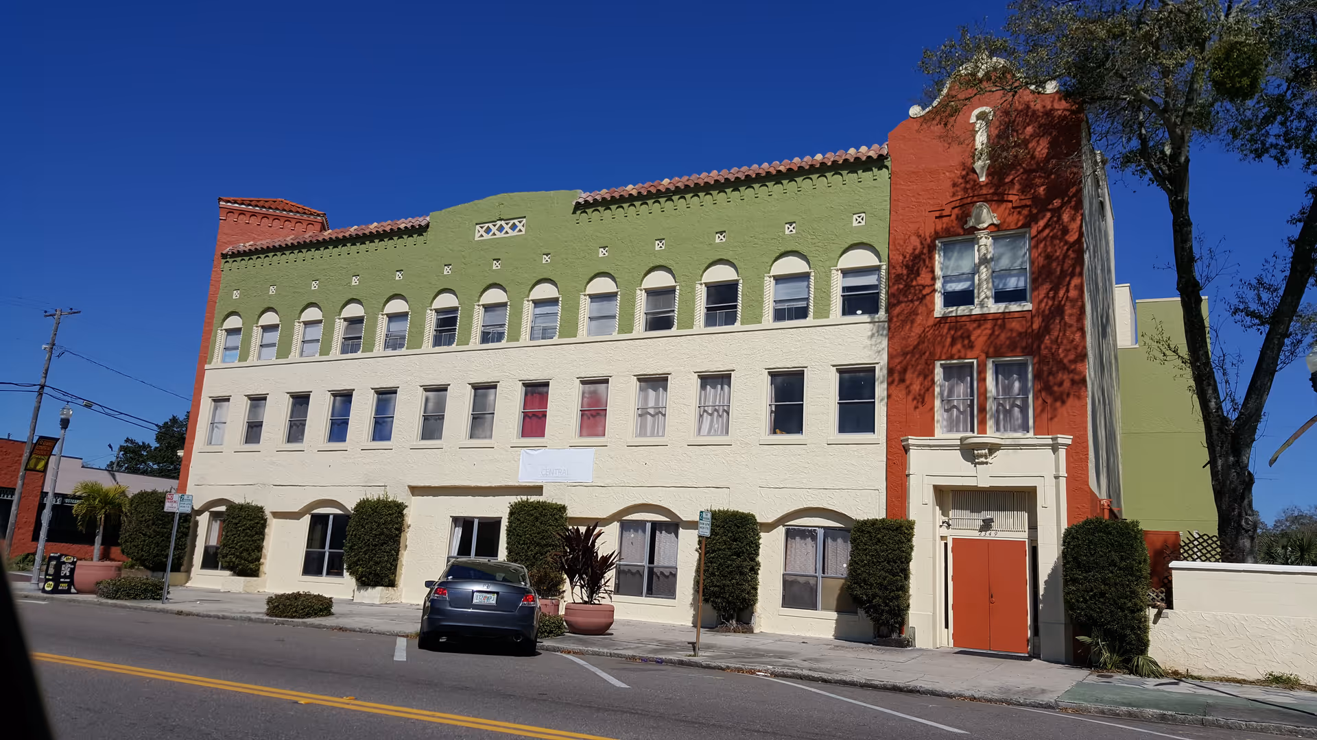 Colorful three-story building with arched windows and a red front entrance on a sunny street.