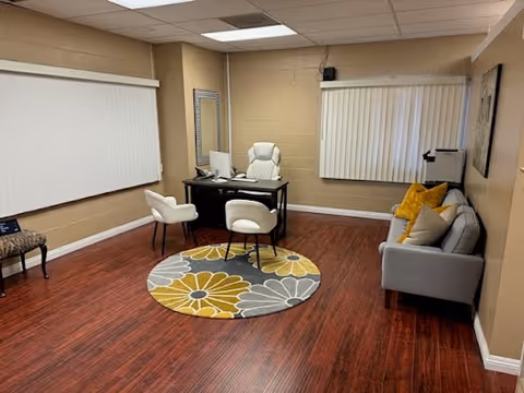 Small beige office area with desk, chairs, sofa, and circular rug.
