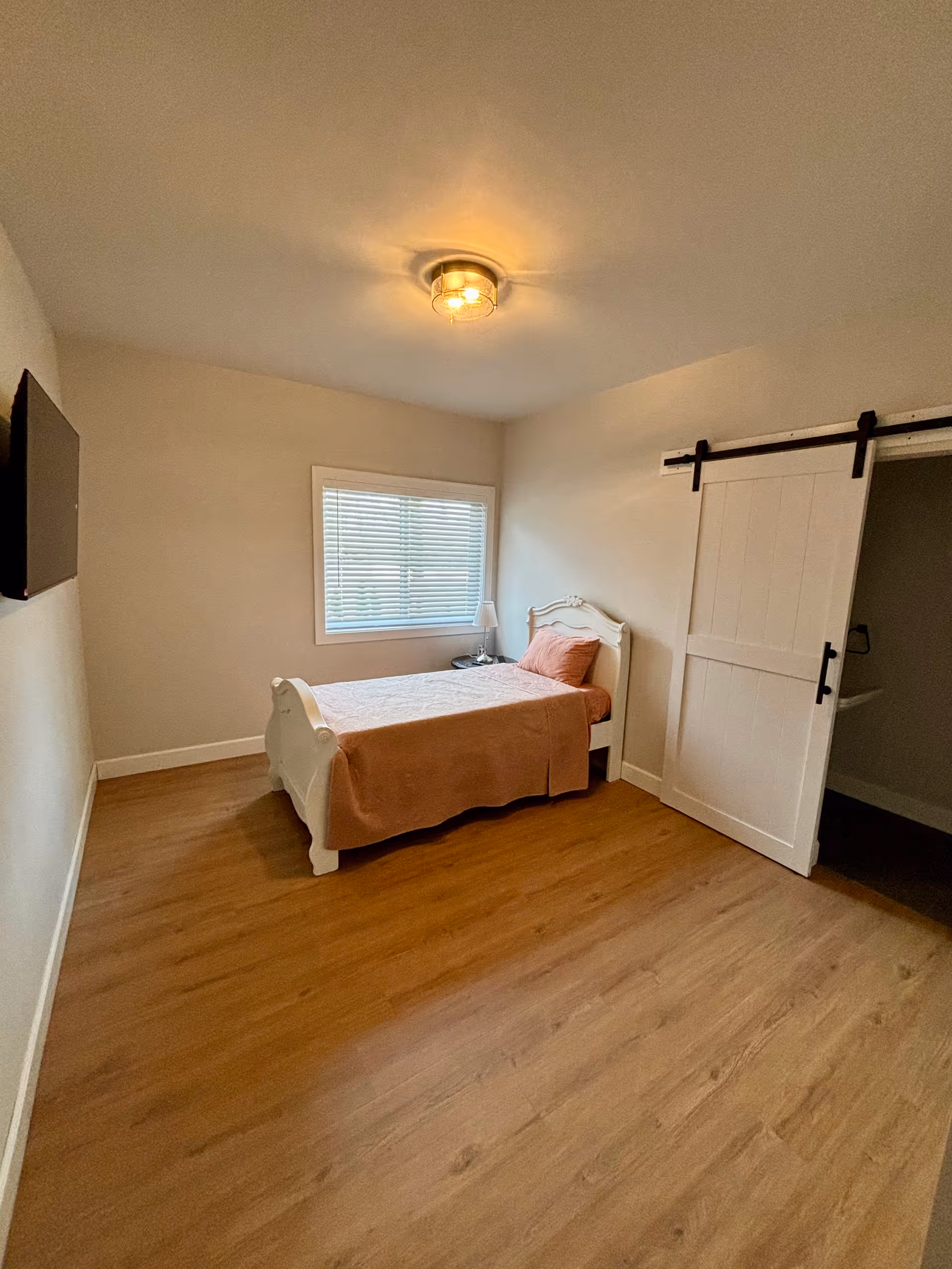 A white single-bed bedroom with peach bedding, window, and sliding barn-door closet.