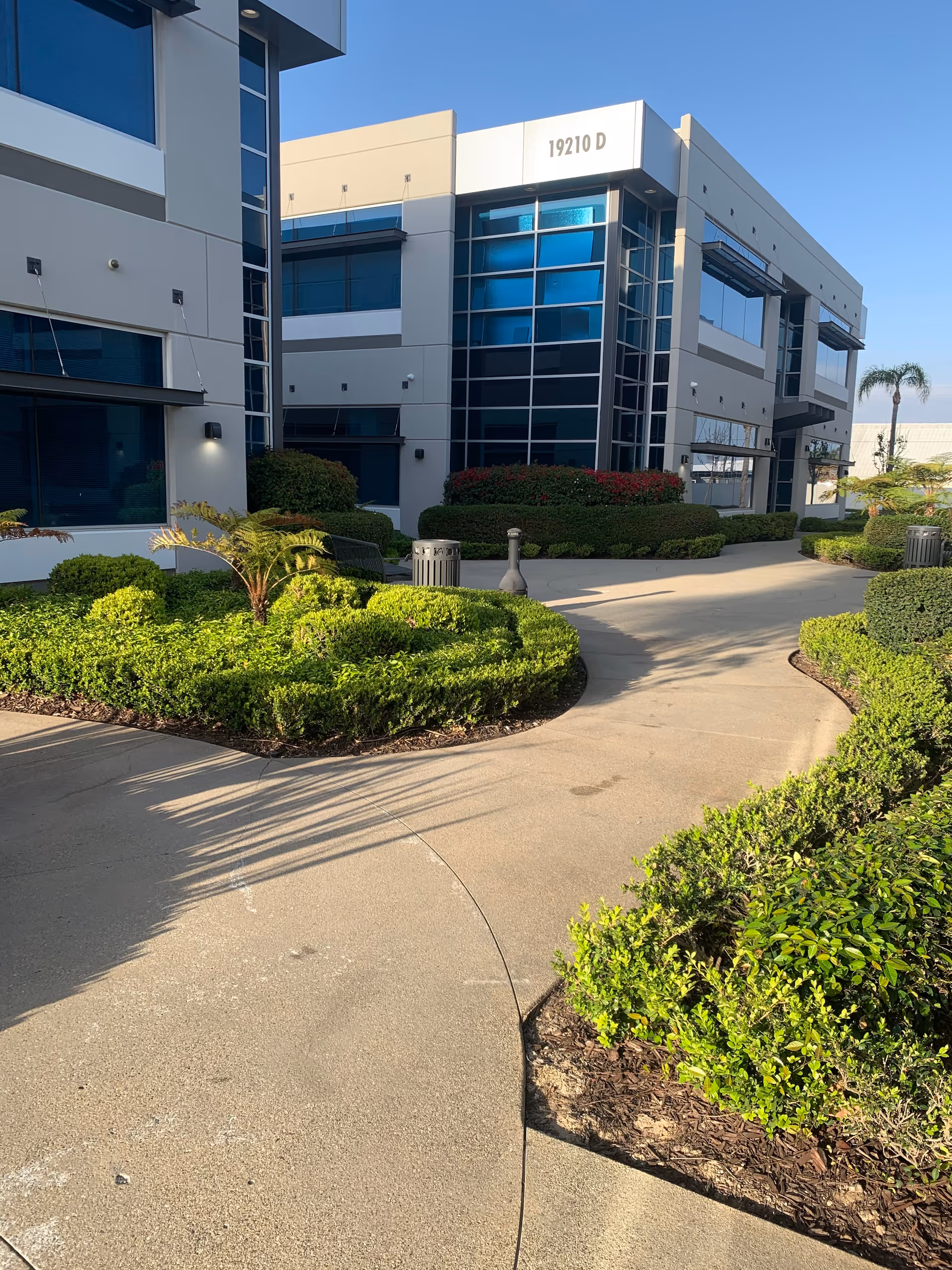 Exterior view of a modern facility with curved walkway and manicured shrubs.