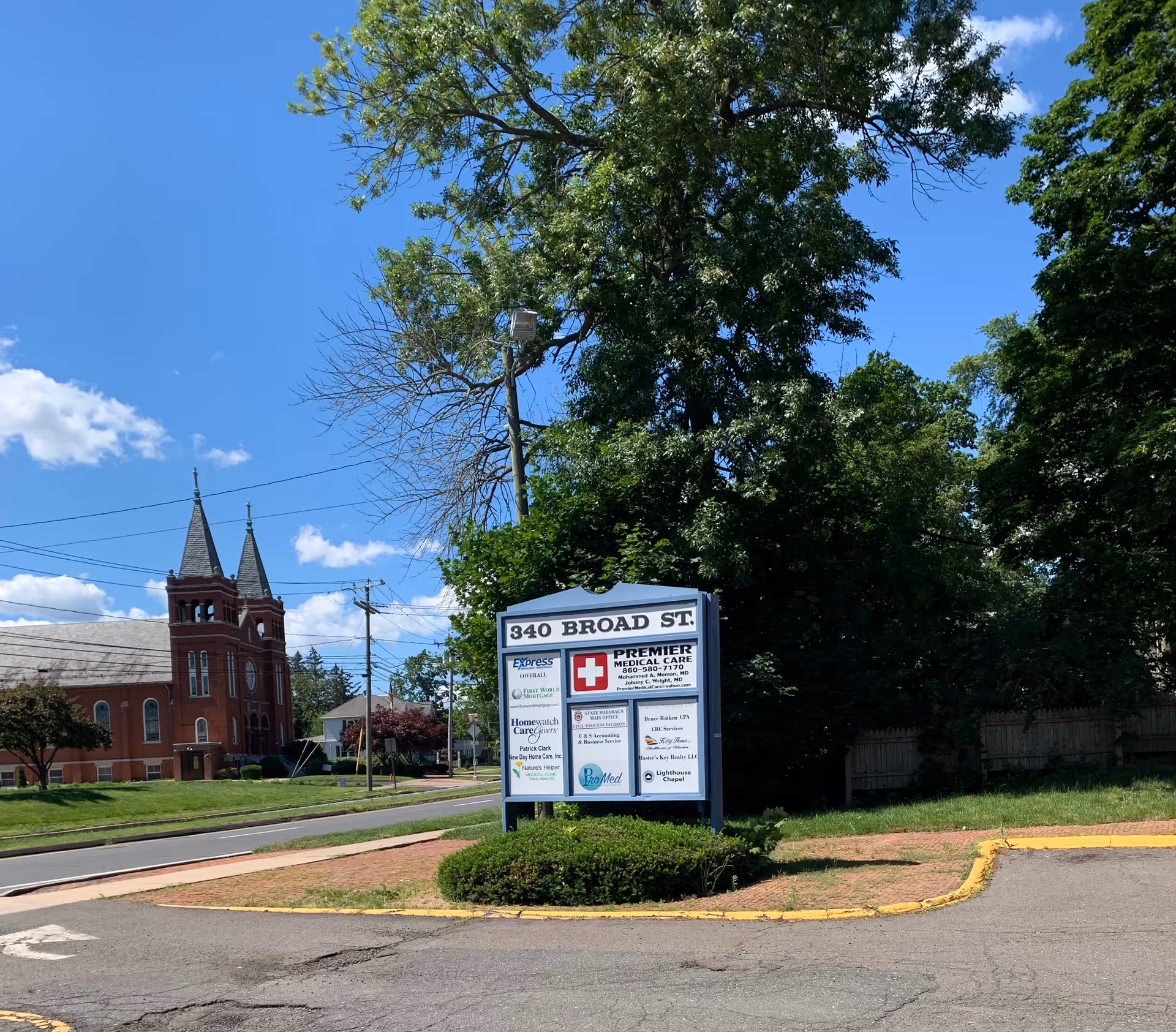 Outdoor directory sign at 340 Broad St surrounded by trees and a brick church.