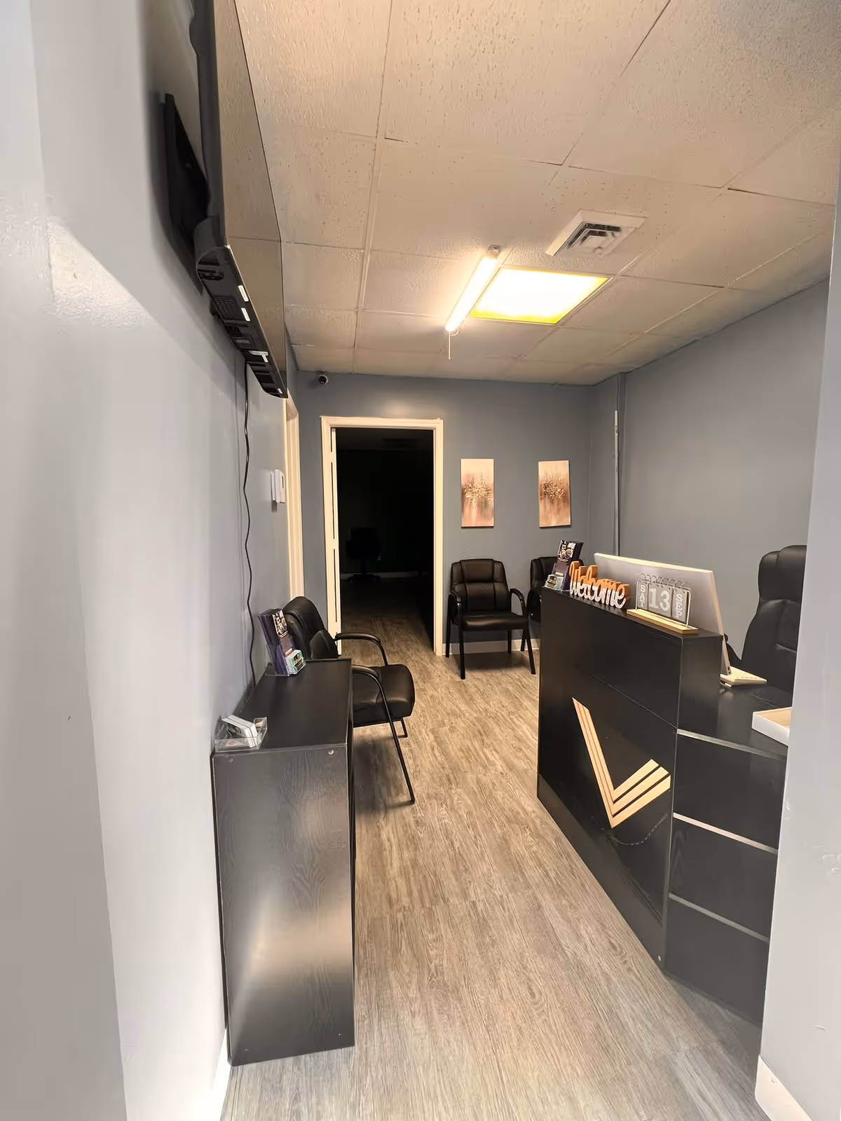 A narrow reception area with a black counter, chairs, and a hallway leading back.