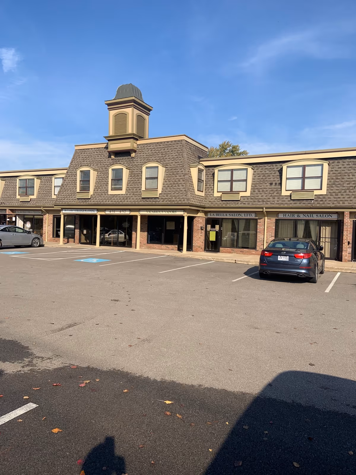 Two-story brick storefront building with arched windows, a cupola, and a parking lot.