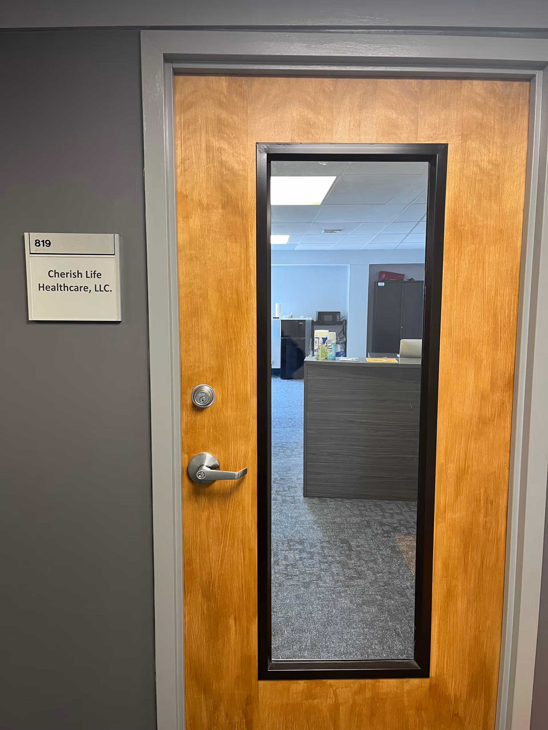 Wooden door with a narrow vertical window opens into an office area and reception desk.